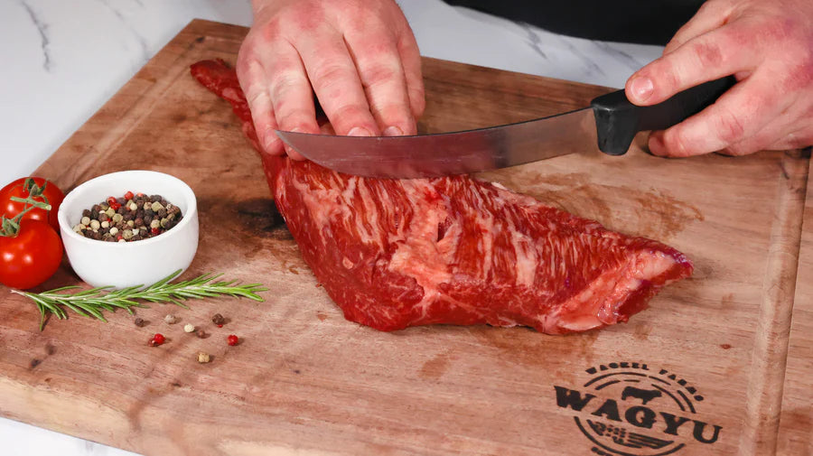 An uncooked tri tip roast with a pronounced triangular shape and straight-grained texture, resting on a wooden cutting board.